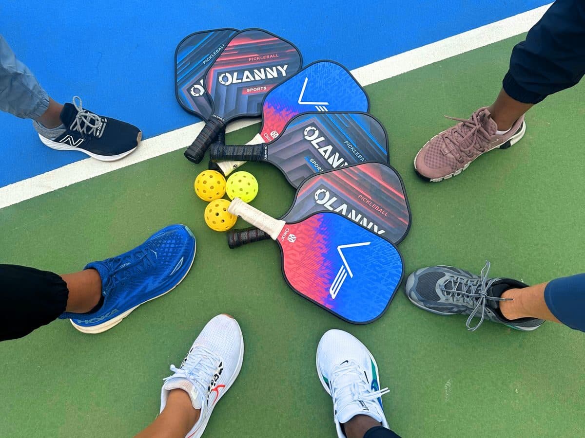 Four players' paddles and balls gathered on an outdoor court before a round robin